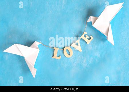 Diffuser le message du concept d'amour. Deux origami colombe blanc portant le mot LOVE sur fond bleu. Banque D'Images