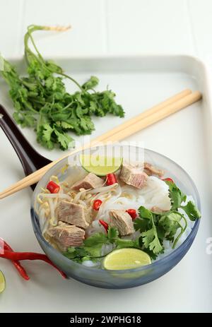 Pho Bo, soupe vietnamienne de nouilles au riz frais avec tranches de bœuf, herbes et Chili. Banque D'Images