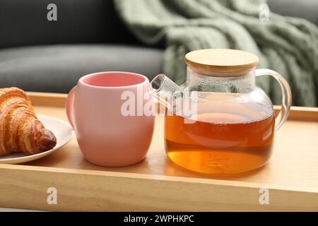 Thé aromatique en théière, tasse et croissant savoureux sur table à l'intérieur Banque D'Images