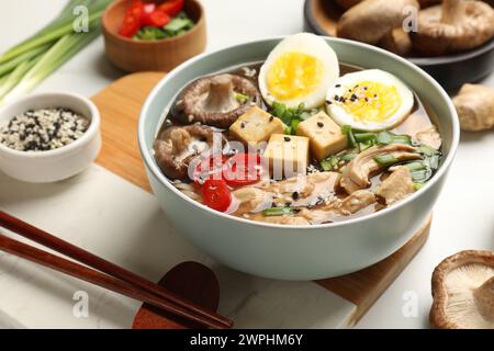 Bol de délicieux ramen et ingrédients sur la table blanche. Soupe de nouilles Banque D'Images