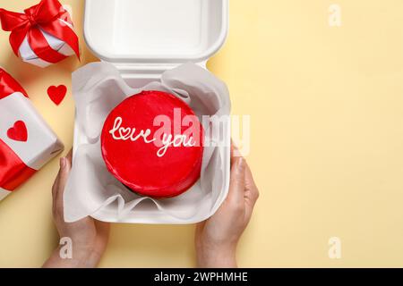 Femme tenant la boîte à emporter avec bento cake à la table beige, vue de dessus. Prog Surprise pour la Saint-Valentin Banque D'Images