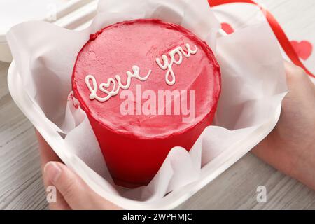 Femme tenant une boîte à emporter avec un gâteau au bento à la table en bois blanc, gros plan. Prog Surprise pour la Saint-Valentin Banque D'Images