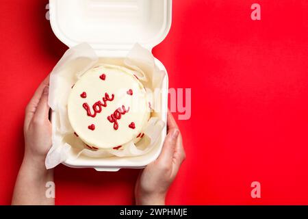 Femme tenant une boîte à emporter avec bento cake à la table rouge, vue de dessus. Prog Surprise pour la Saint-Valentin Banque D'Images