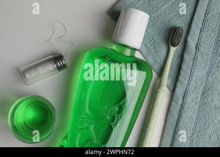 Rince-bouche frais en bouteille, verre, brosse à dents et fil dentaire sur fond clair, plat Banque D'Images