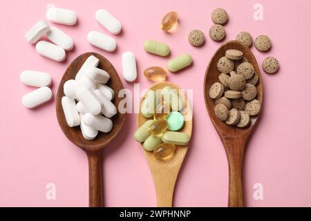 Différentes pilules de vitamines dans des cuillères en bois sur fond rose, plat Banque D'Images