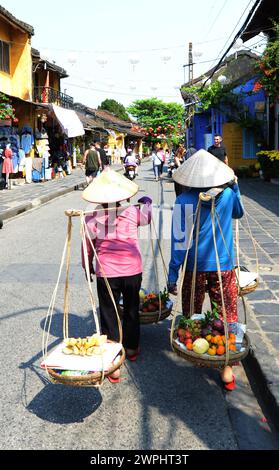 Les femmes vietnamiennes marchant avec le poteau de transport avec des paniers avec des fruits, également appelé un poteau d'épaule, à Hoi an, Vietnam. Banque D'Images