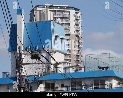 TOKYO, JAPON - 7 mars 2024 : poteau électrique et lignes électriques dans le quartier Yayoi de Tokyo avec le sommet d'un immeuble des années 1960 derrière. Banque D'Images