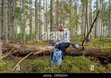 Femme prenant un café assis sur une bûche dans la forêt Banque D'Images