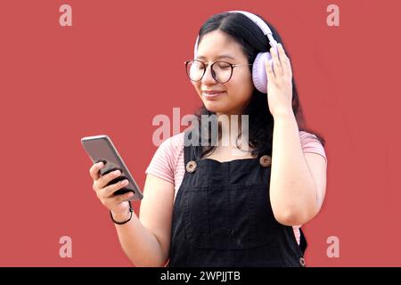 Une adolescente Latina de 17 ans utilise son téléphone portable et audio pour se connecter à de la musique, des livres audio podcast et des chansons avec ses amis Banque D'Images