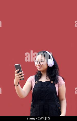 Une adolescente Latina de 17 ans utilise son téléphone portable et audio pour se connecter à de la musique, des livres audio podcast et des chansons avec ses amis Banque D'Images