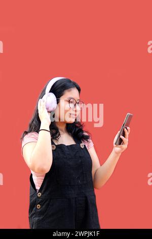 Une adolescente Latina de 17 ans utilise son téléphone portable et audio pour se connecter à de la musique, des livres audio podcast et des chansons avec ses amis Banque D'Images