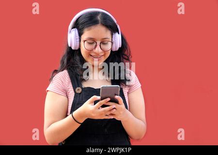 Une adolescente Latina de 17 ans utilise son téléphone portable et audio pour se connecter à de la musique, des livres audio podcast et des chansons avec ses amis Banque D'Images