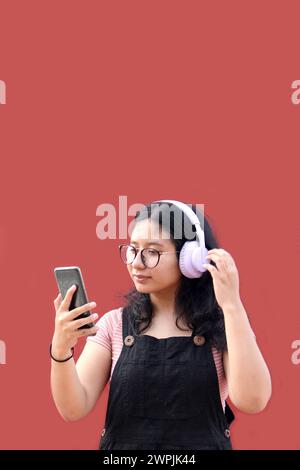 Une adolescente Latina de 17 ans utilise son téléphone portable et audio pour se connecter à de la musique, des livres audio podcast et des chansons avec ses amis Banque D'Images