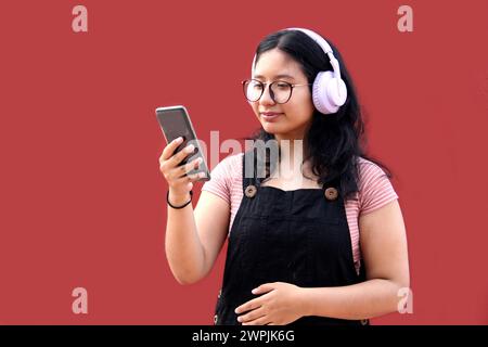 Une adolescente Latina de 17 ans utilise son téléphone portable et audio pour se connecter à de la musique, des livres audio podcast et des chansons avec ses amis Banque D'Images