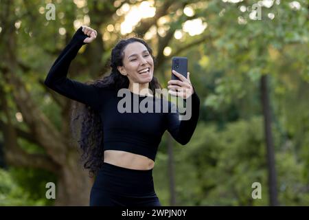 Une femme souriante et active en tenue athlétique capture un moment joyeux sur son téléphone, incarnant la santé et le bonheur. Banque D'Images