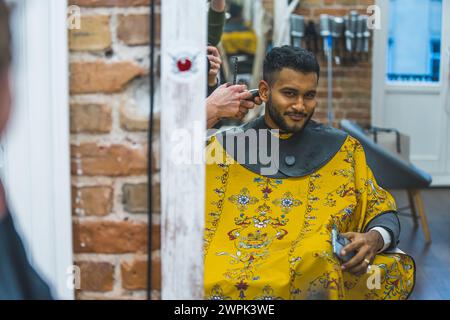 Sourire client reflet dans le miroir assis sur une chaise de barbier tout en obtenant ses cheveux taillés . Photo de haute qualité Banque D'Images