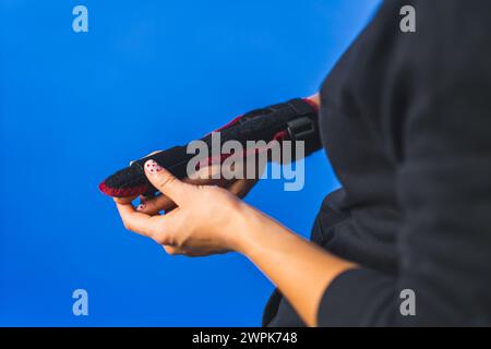 femme ajustant une attelle sur son majeur, doigt blessé fond bleu. Photo de haute qualité Banque D'Images