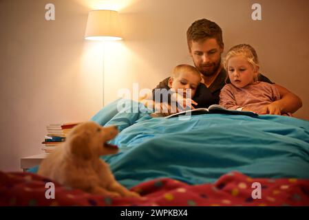 Nuit, enfants ou père lisant livre au lit pour l'apprentissage, l'éducation ou la narration à la maison avec chien. Famille, détente ou papa avec des frères et sœurs pour un plaisir Banque D'Images