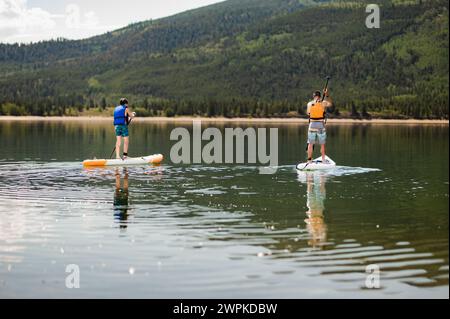 Deux paddleboarders profitent d'une pagaie sereine sur un lac de montagne calme Banque D'Images