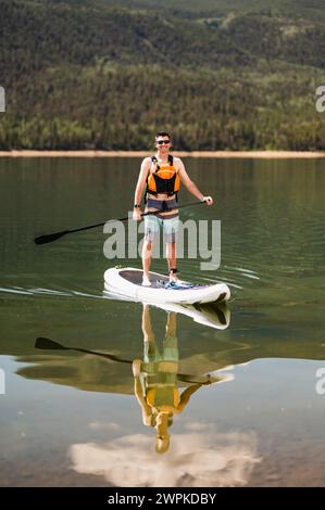 Homme profitant d'une séance de paddleboard ensoleillé sur un lac de montagne calme Banque D'Images