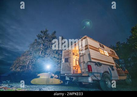 Femme assise sur la table de pique-nique à côté du camping-car pendant le voyage de surf Banque D'Images