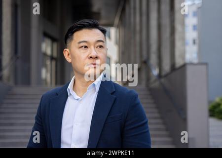 Un homme d'affaires asiatique professionnel à l'extérieur dans un environnement urbain, regardant avec soin avec confiance. Banque D'Images