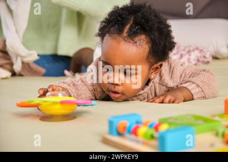 Bébé cubain jeune fille essayant d'atteindre un jouet jouant sur le lit à la maison. Banque D'Images