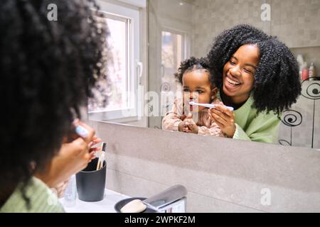 Mère cubaine brossant les dents de sa petite fille et riant. Banque D'Images