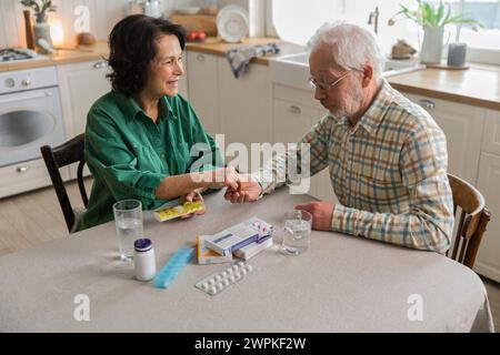 femme âgée donne des médicaments au vieux mari souriant Banque D'Images