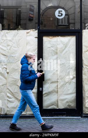 Une femme envoyant un SMS sur son téléphone portable passant devant un magasin fermé dans le centre-ville de Newquay en Cornouailles au Royaume-Uni. Banque D'Images