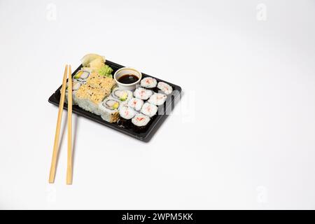 Sushi à emporter dans une boîte noire à emporter avec des baguettes en bois sur fond blanc Banque D'Images
