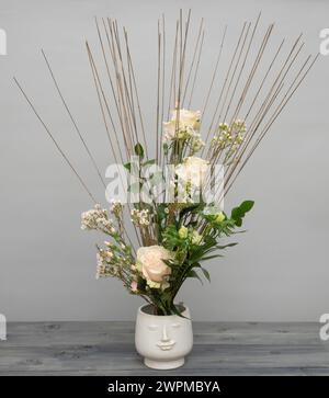 Bouquet noué à la main avec des roses roses, des fleurs de cire, du dianthus et des anémones sur un cadre en bâton de roseau, dans une jardinière à visage blanc. Banque D'Images