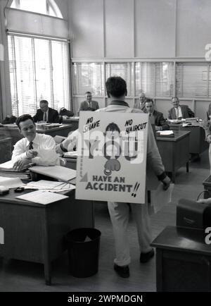 Années 1950, historique, dans un bureau d'administration à la papeterie Camas, un homme portant un panneau sandwich, avec un message de sécurité sur le dos.... 'Pas de rasage, pas de coupe de cheveux... Jusqu'à ce que vous ayez un accident', un employé de l'entreprise connu sous le nom de l'homme de sécurité, qui ferait le tour de l'usine industrielle pour promouvoir la sécurité sur le site..... À l'intérieur du bureau, un collègue distribuait des dépliants de sécurité aux employés de bureau assis à leur bureau, WA, États-Unis. Banque D'Images