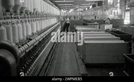 Années 1950, historique, un opérateur masculin - ou Minder comme ils étaient connus - travaillant sur l'étage d'usine d'une grande usine de coton, supervisant le grand nombre de mules filantes, États-Unis. L'invention de la mule de filature en 1779 et la révolution industrielle ont transformé la production de textiles. Banque D'Images