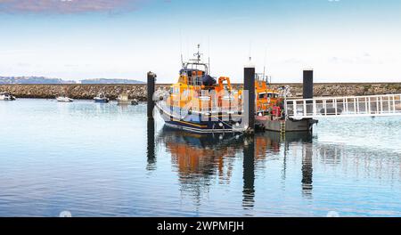 Torbay Lifeboat amarré à Brixham Marina Devon près du brise-lames et de la passerelle d'accès au canot de sauvetage et aux reflets dans l'eau avec une ligne d'horizon lointaine Banque D'Images