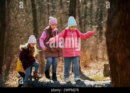 Petits enfants en tenue d'hiver jouant et en équilibre sur le tronc d'arbre tombé. Activité de loisirs. Activités de plein air pour le développement des enfants. Banque D'Images