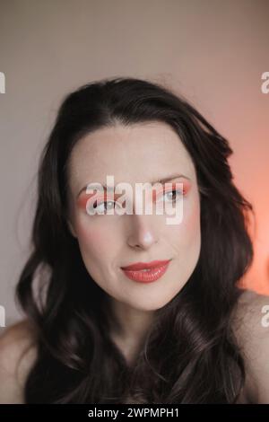 Portrait d'une jeune femme vêtue de maquillage dans les tons rouge et pêche avec ses cheveux foncés vers le bas Banque D'Images