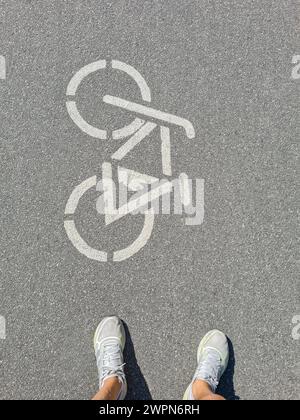 Jambes de femmes avec des chaussures de sport blanches devant le pictogramme de vélo sur une piste cyclable en Allemagne Banque D'Images