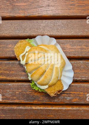 Un rouleau de poisson en forme de moule surmonté de poisson frit et de sauce tartare dans une boîte en carton sur une table en bois Banque D'Images