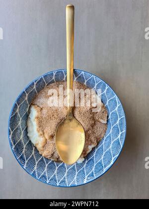 Pudding de riz à la cannelle et au sucre dans un bol bleu sur fond gris à la lumière du jour Banque D'Images