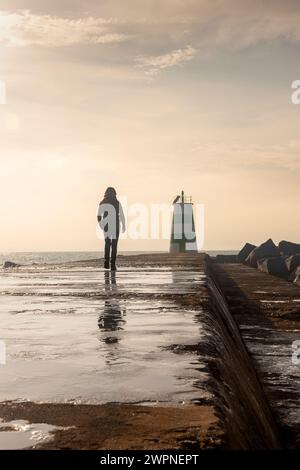 Silhouette d'une personne marchant vers un phare le long du brise-lames Banque D'Images