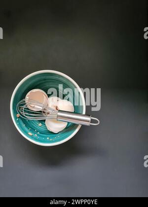 Les coquilles d'œufs et le fouet sont placés dans un bol vert avec un bord blanc Banque D'Images