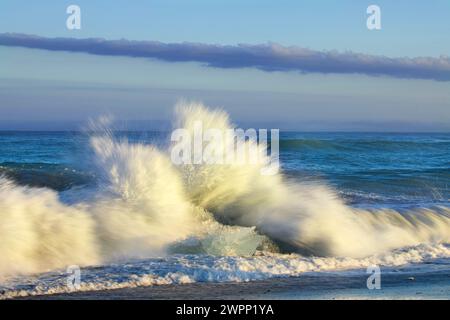 Les vagues de l'Atlantique se brisent sur des blocs de glace échoués sur la plage de Diamond Beach dans le sud de l'Islande. Banque D'Images