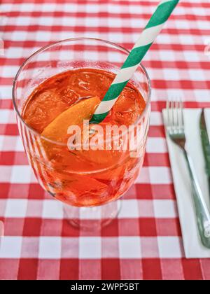 Une boisson d'été alcoolisée de couleur orange avec une tranche d'orange et de la paille dans le verre se tient sur une nappe rouge et blanche Banque D'Images