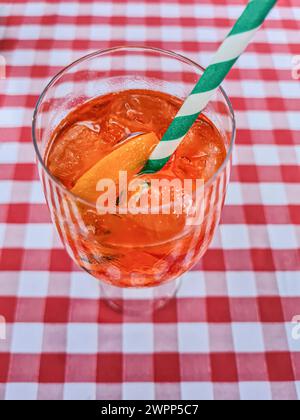 Une boisson d'été alcoolisée de couleur orange avec une tranche d'orange et de la paille dans le verre se tient sur une nappe rouge et blanche Banque D'Images