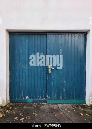 Mur blanc avec portail en bois bleu et poignée de porte, feuilles d'automne sur le sol, Allemagne Banque D'Images