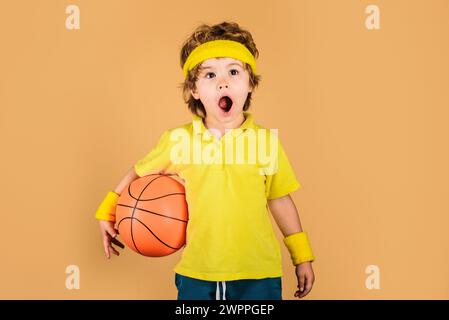 Garçon enfant surpris en uniforme de sport avec ballon de basket-ball. Petit joueur de basket-ball en sportswear avec balle. Adorable enfant jouant au basket-ball. Sport Banque D'Images