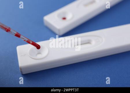 Déposer l'échantillon de sang sur une cassette de test express jetable avec une pipette sur fond bleu, gros plan Banque D'Images