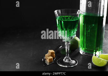 Absinthe, cuillère, cassonade et citron vert sur table noire, espace pour le texte. Boisson alcoolisée Banque D'Images