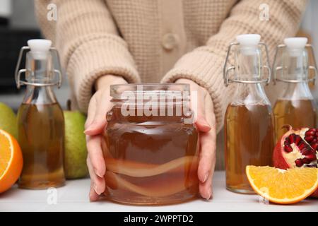 Femme prenant pot de kombucha fermenté maison à table blanche, gros plan Banque D'Images